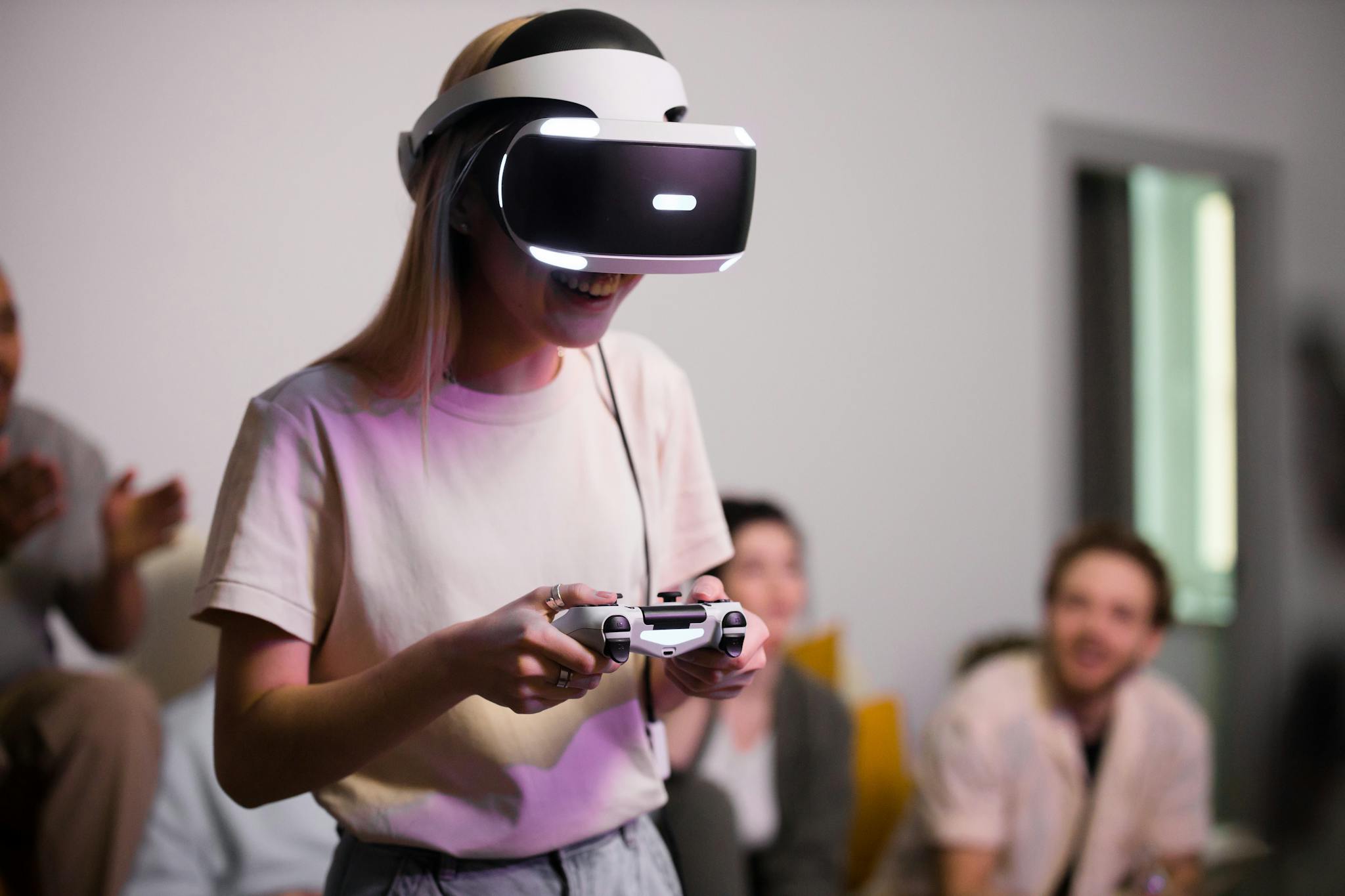 Smiling woman wearing VR headset and holding a gaming controller indoors with friends.